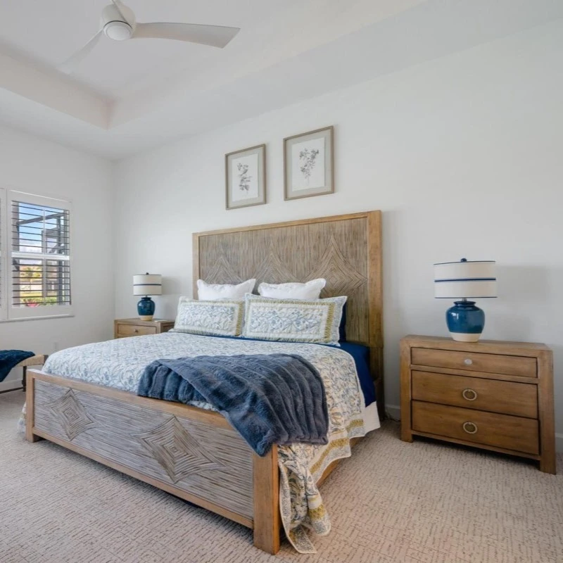 a bedroom with a bed that ahs blue and white covers, as well as two wooden night stands with blue and white lamps.